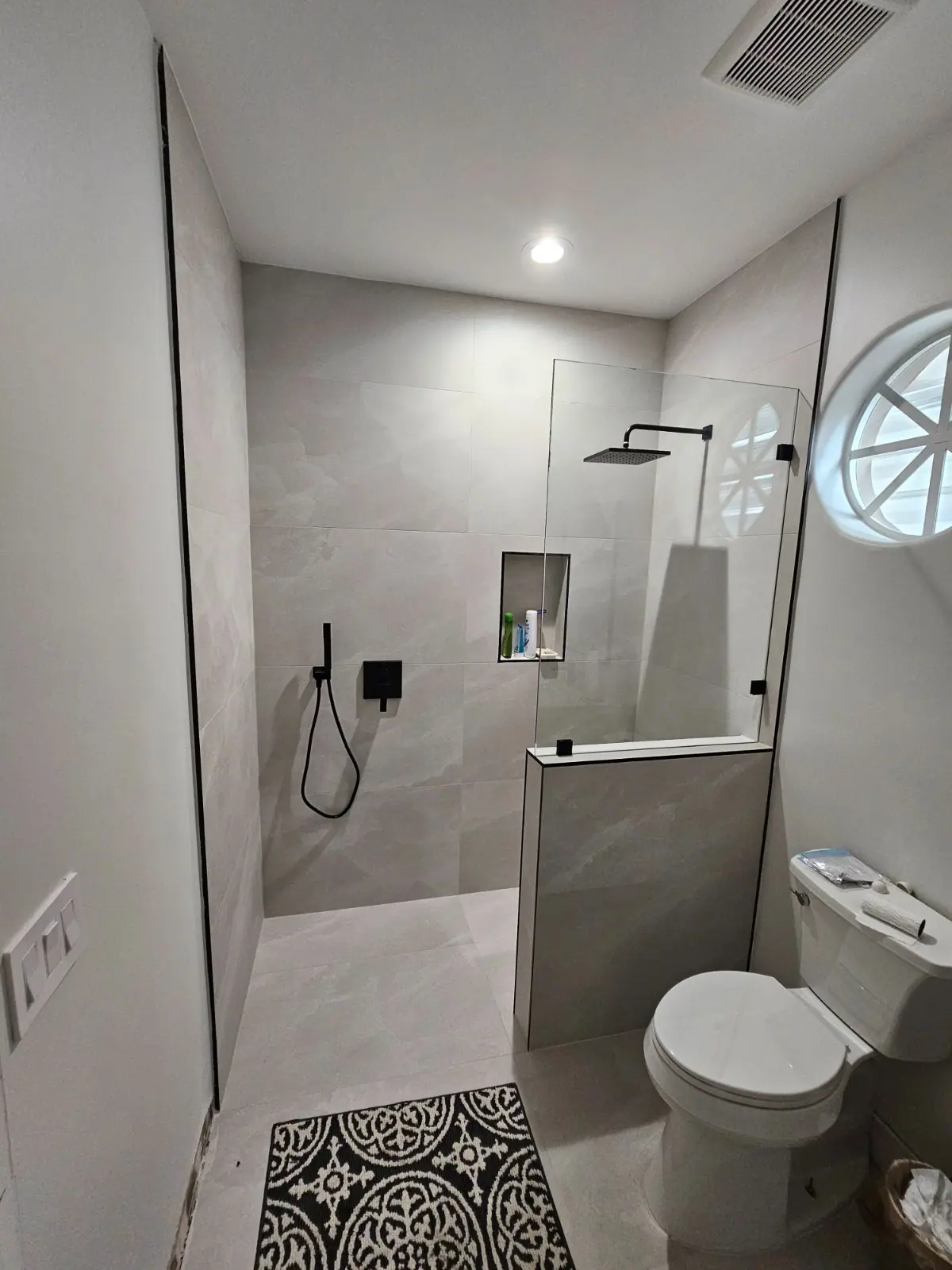 Gray tiled bathroom with black fixtures and glass shower enclosure