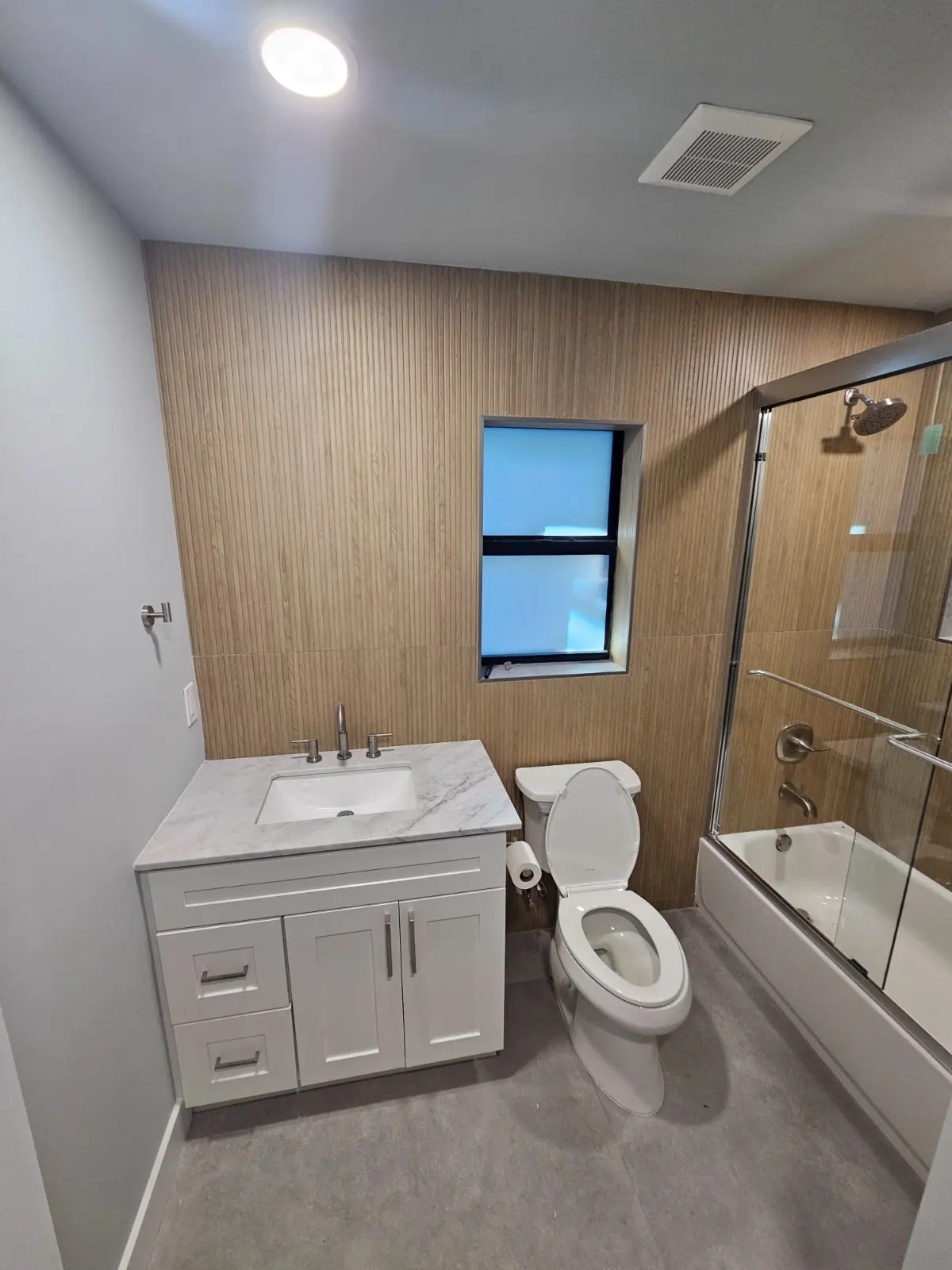 Bathroom with white vanity, wood-look tile wall and glass shower