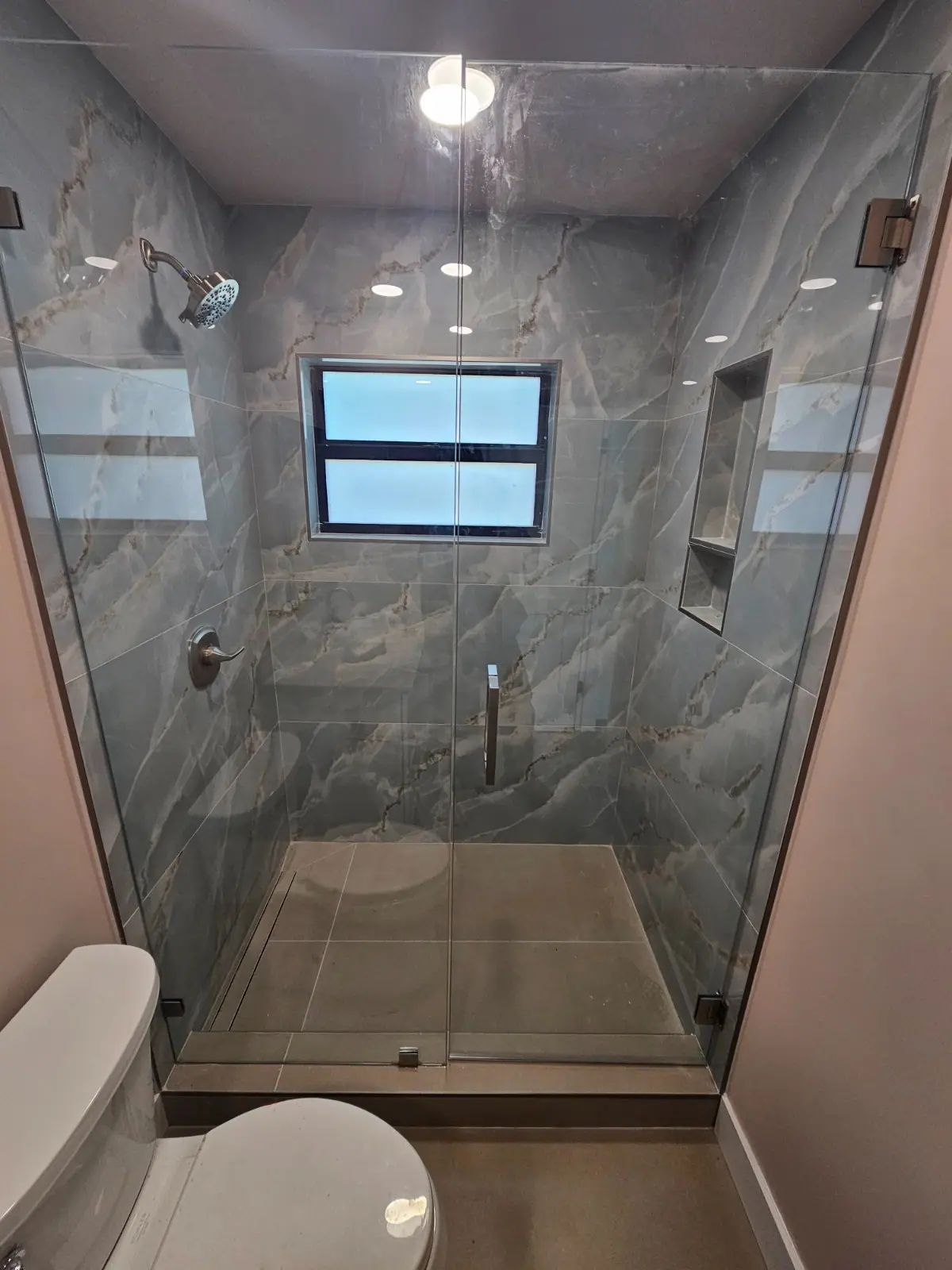 Gray stone shower with glass enclosure and recessed niche