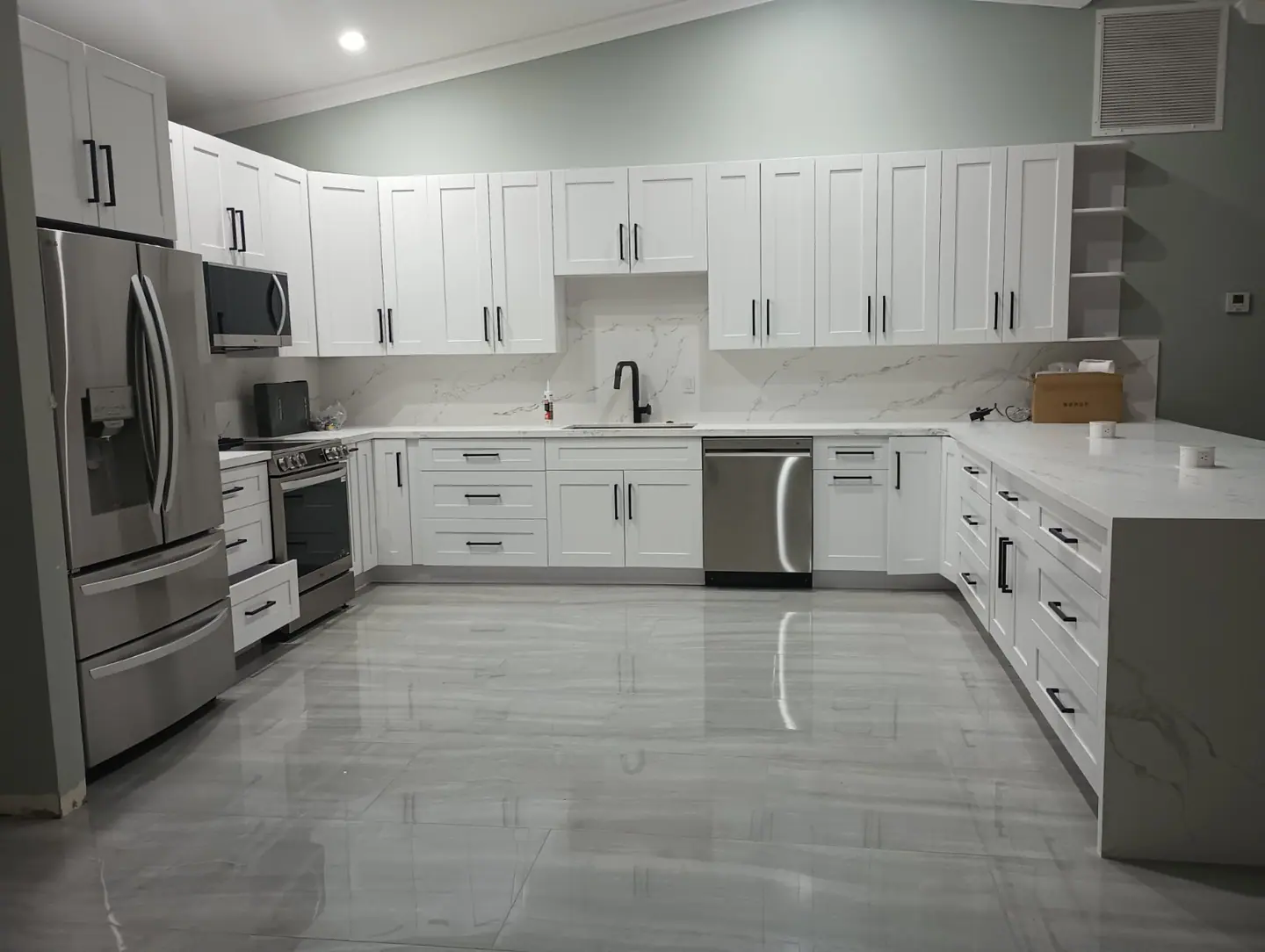 White custom kitchen with black hardware, marble counters and glossy tile floor
